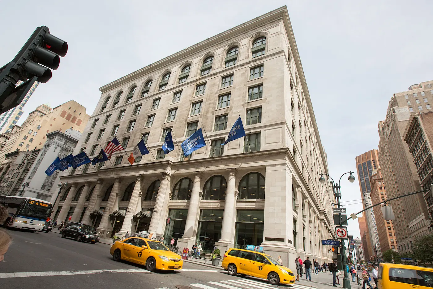 Exterior of the CUNY Graduate Center building - flags on building, taxis and vehicles on the street.